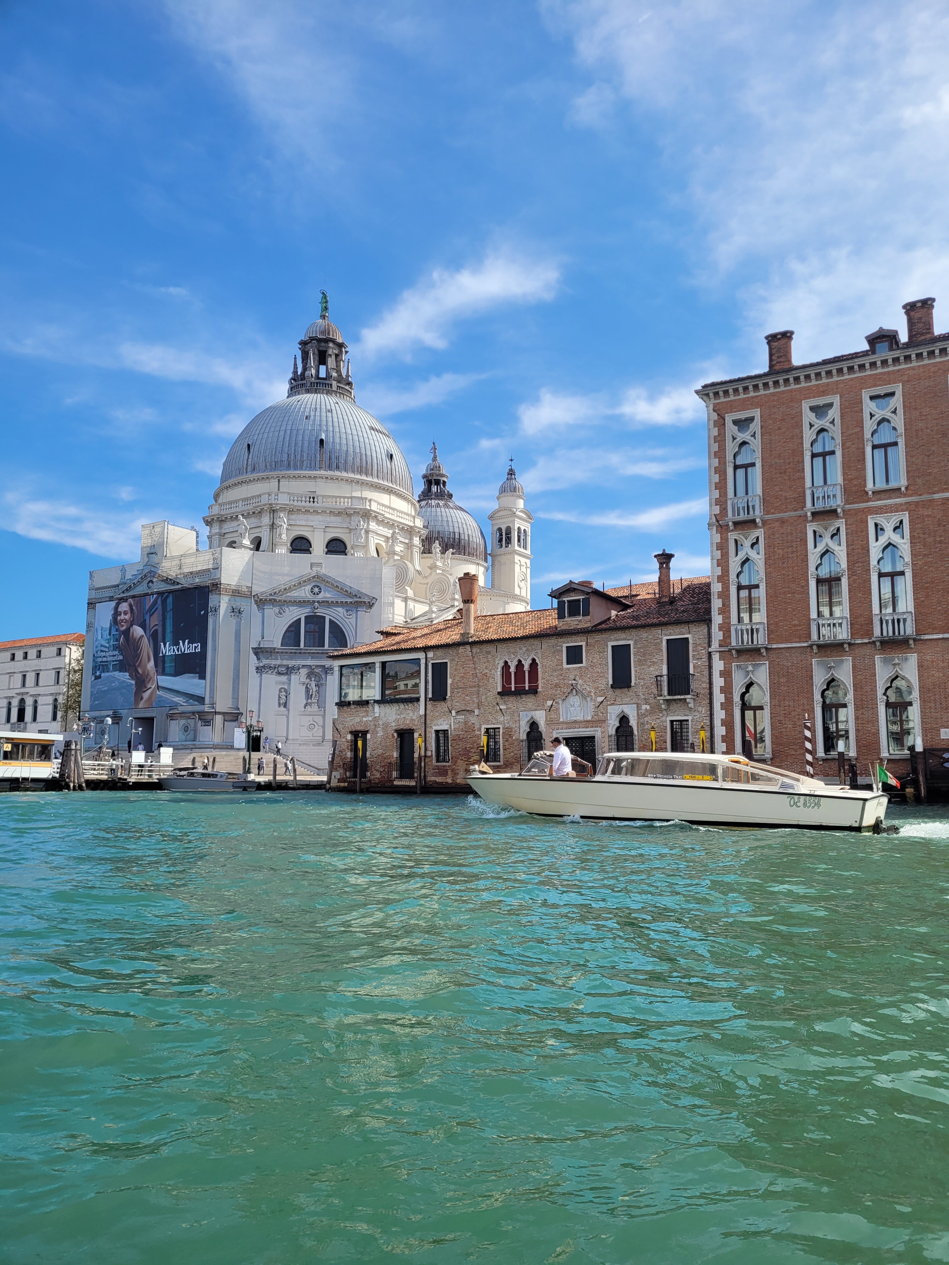 Venetian architecture with a domed building reflected in the water, under a blue sky.